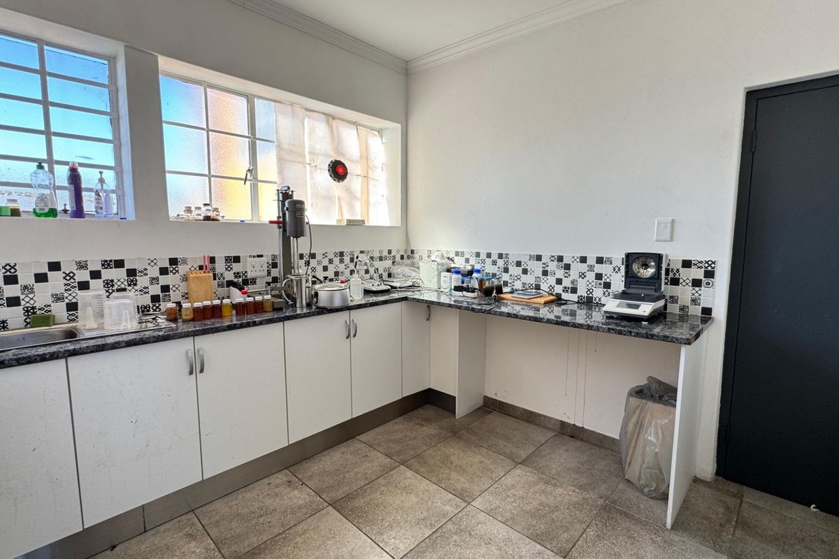 A functional industrial kitchen area featuring granite-look countertops, white cabinetry, tiled backsplash, and large windows providing natural light.