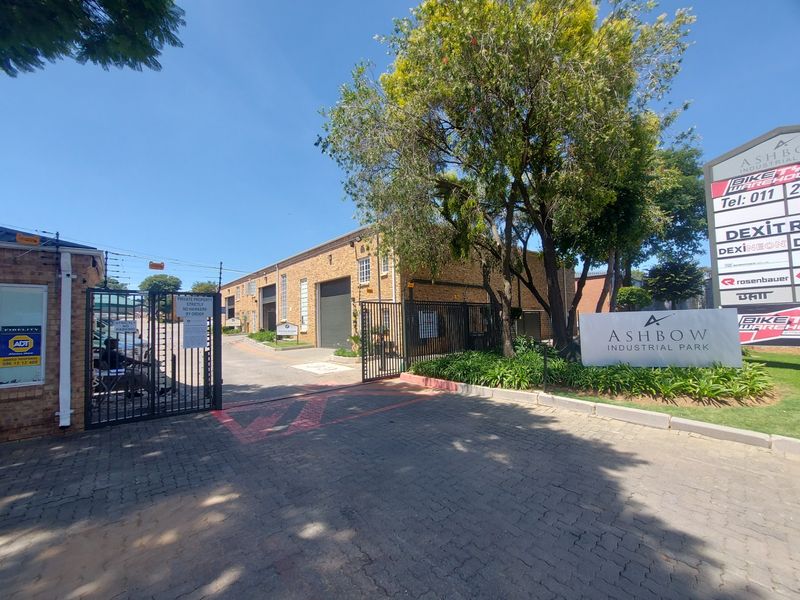 Entrance view of Ashbow Industrial Park featuring a paved driveway, secure gated access, brick industrial buildings, and prominent business signage.