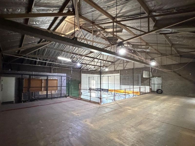 Spacious industrial mezzanine area featuring exposed steel roof trusses, concrete flooring, and metal mesh partitioning, suitable for storage or workshop use.