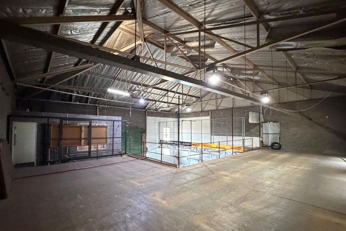 Spacious industrial mezzanine area featuring exposed steel roof trusses, concrete flooring, and metal mesh partitioning, suitable for storage or workshop use.