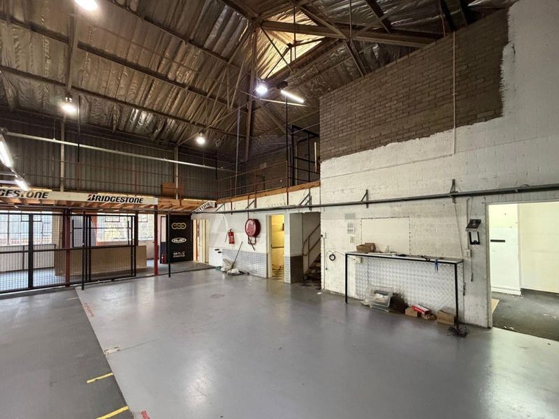 Spacious industrial utility area featuring high ceilings with exposed steel trusses, a mezzanine level, and durable epoxy flooring, suitable for various commercial uses.