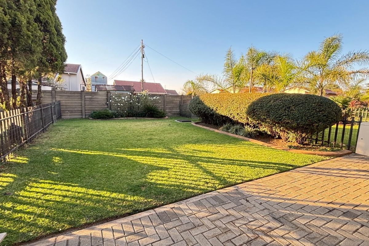 A well-maintained rear garden featuring a manicured lawn, paved patio area, and established perimeter hedging and fencing.