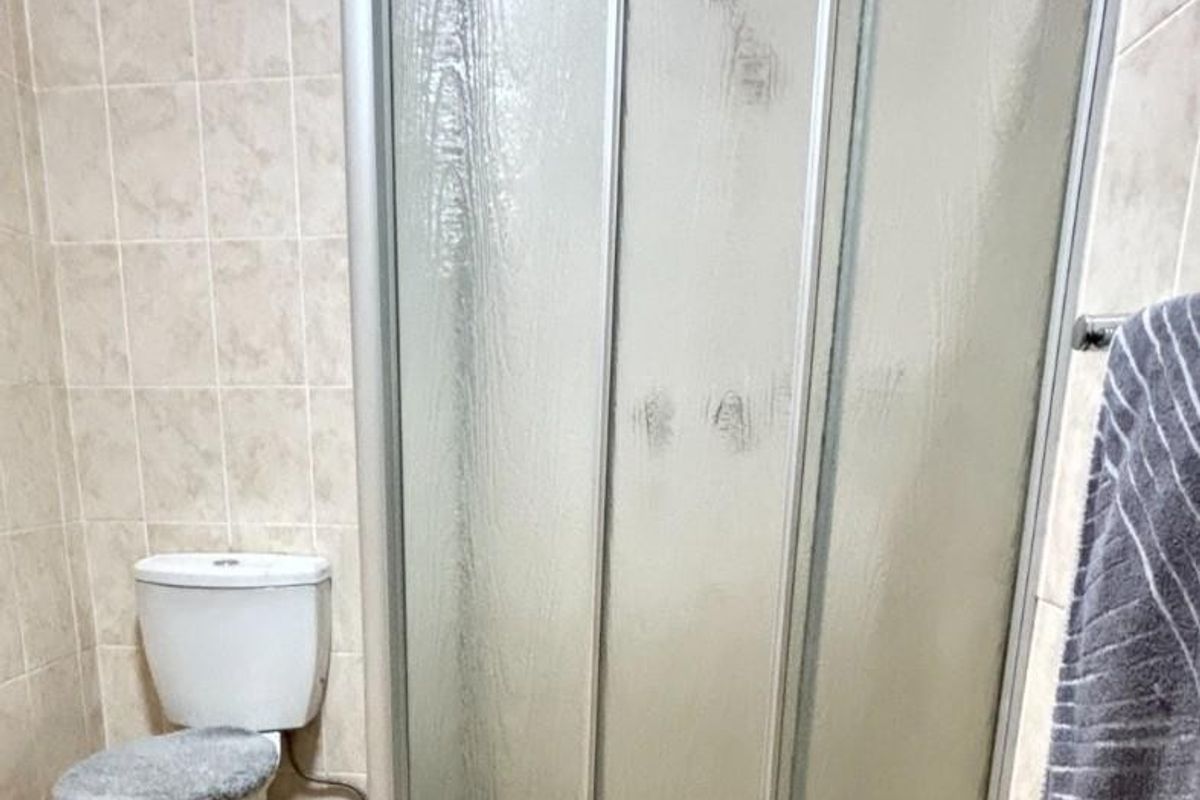 A functional bathroom featuring a corner shower enclosure with sliding doors and a standard toilet, finished with neutral wall and floor tiling.