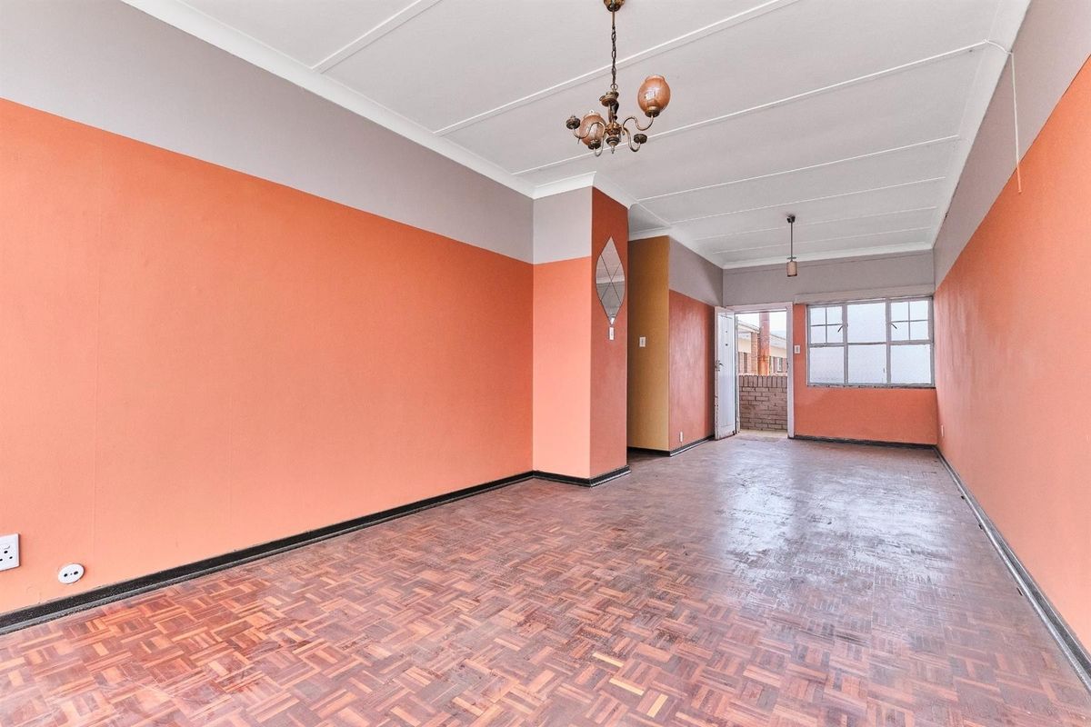 An empty living area featuring original parquet flooring, high ceilings with decorative lighting, and access to an exterior balcony area.