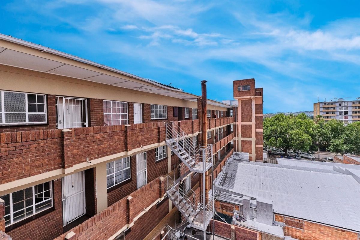 Exterior view of a multi-story apartment building featuring face-brick facade, external metal fire escape staircase, and security gates on unit entrances.