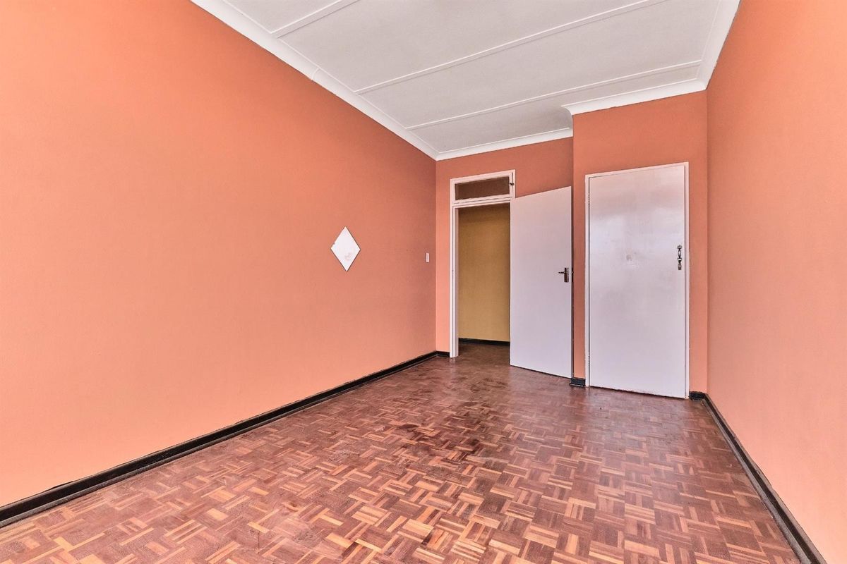 An empty bedroom featuring traditional parquet flooring, painted walls, and a standard door leading to an adjacent space.