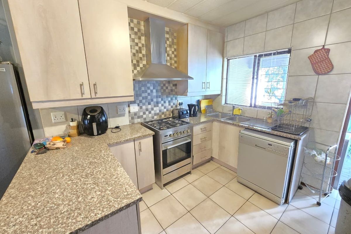 Functional kitchen featuring light-toned cabinetry, granite-look countertops, stainless steel gas stove with extractor fan, and tiled flooring.