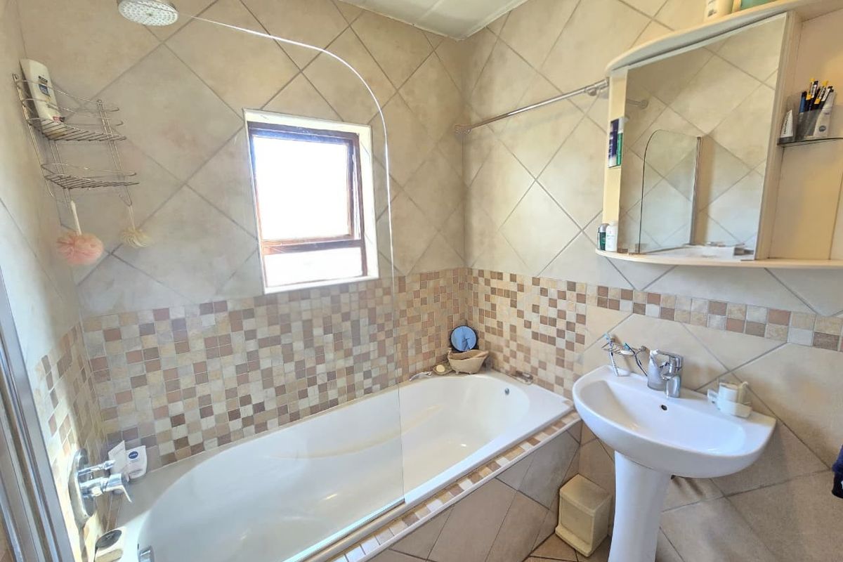 A functional bathroom featuring a bathtub with an integrated shower, a pedestal basin, and a mirrored medicine cabinet with tiled walls.