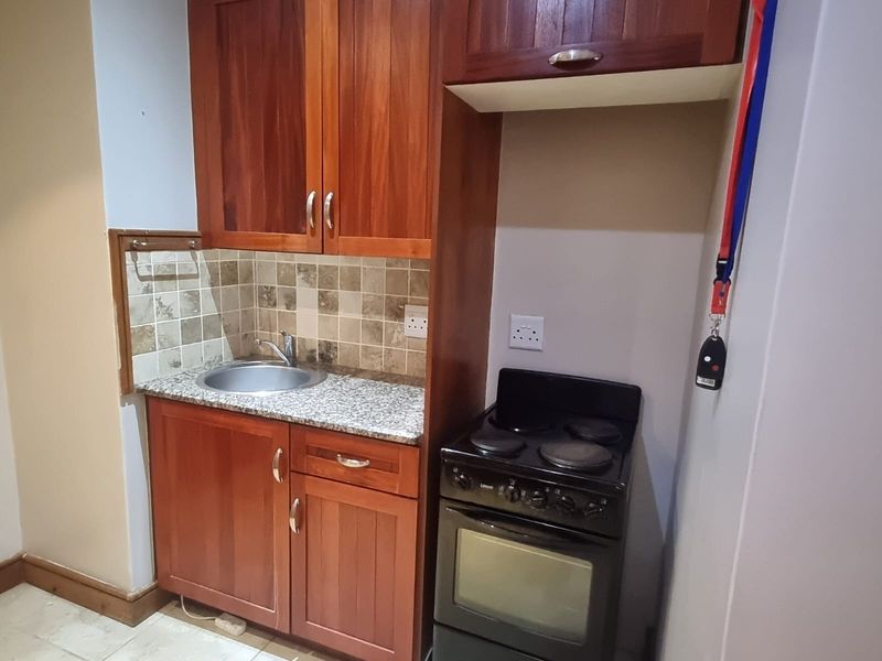 Compact kitchen featuring wooden cabinetry, granite countertops, tiled splashback, and a freestanding electric stove, providing essential functionality in a retirement village setting.