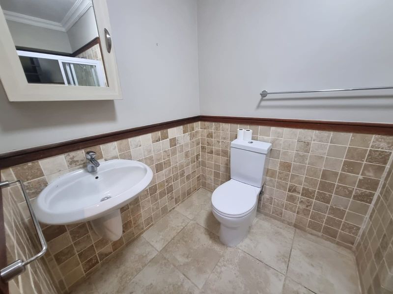 A functional bathroom featuring a pedestal washbasin, toilet, and neutral tiled finishes with a wall-mounted mirror and towel rail.