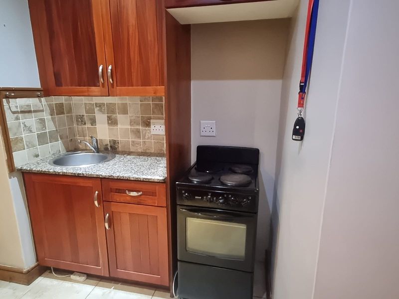 Compact kitchen featuring wooden cabinetry, granite countertops, a tiled backsplash, and a freestanding electric stove.