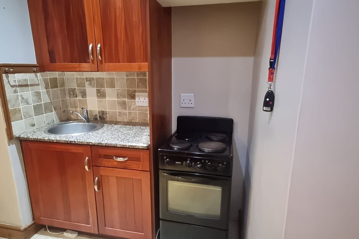 Compact kitchen featuring wooden cabinetry, granite countertops, a tiled backsplash, and a freestanding electric stove.