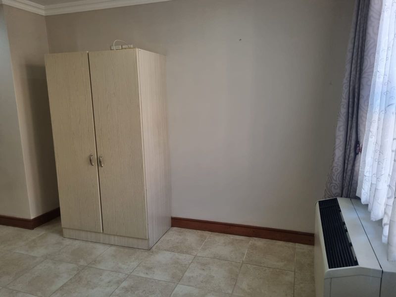 A bedroom featuring tiled flooring, coving, a built-in wardrobe, and a wall-mounted HVAC unit.