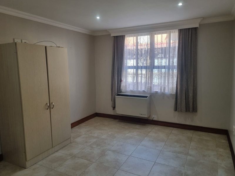 A functional bedroom featuring tiled flooring, recessed downlighting, and a wall-mounted air conditioning unit, providing a neutral space ready for personalization.