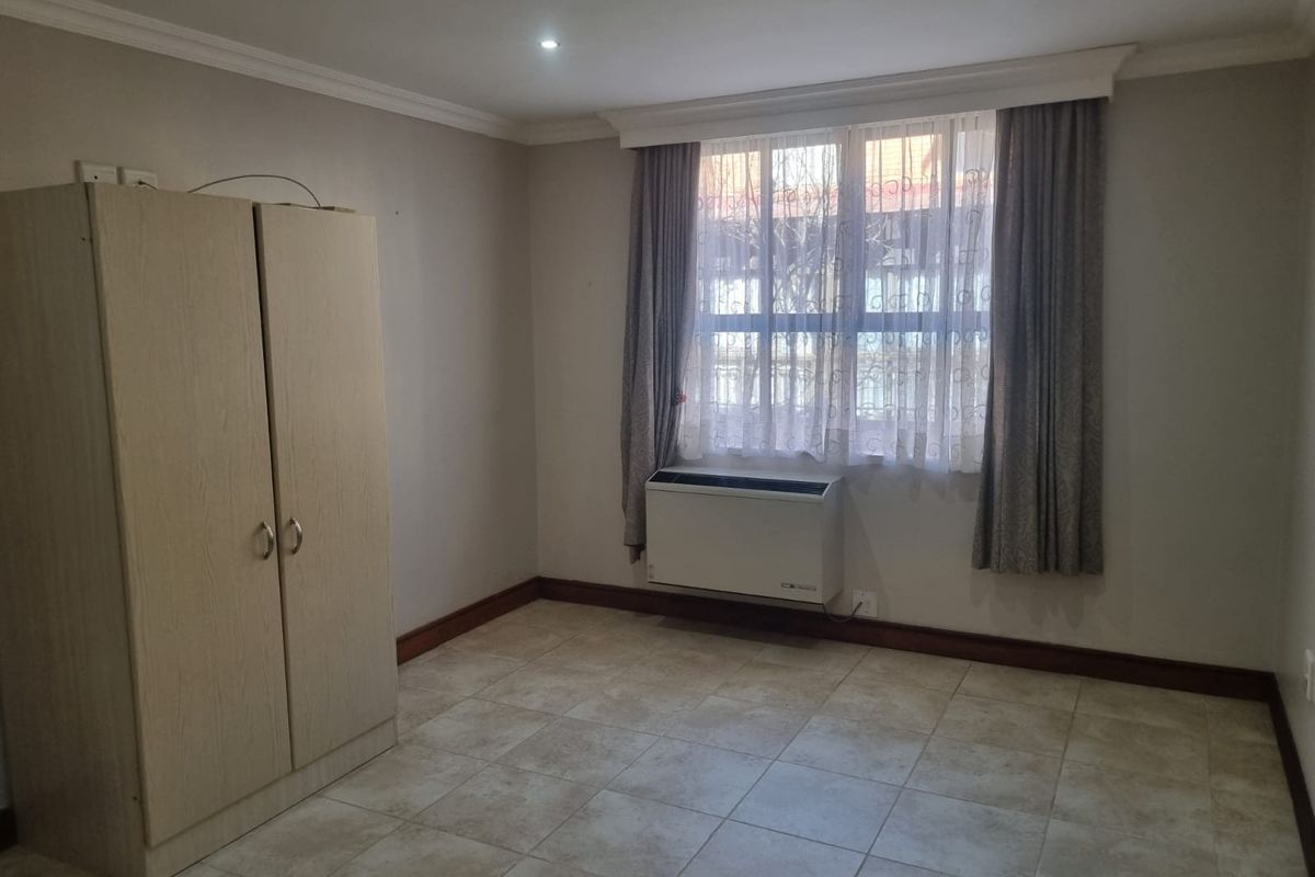 A functional bedroom featuring tiled flooring, recessed downlighting, and a wall-mounted air conditioning unit, providing a neutral space ready for personalization.
