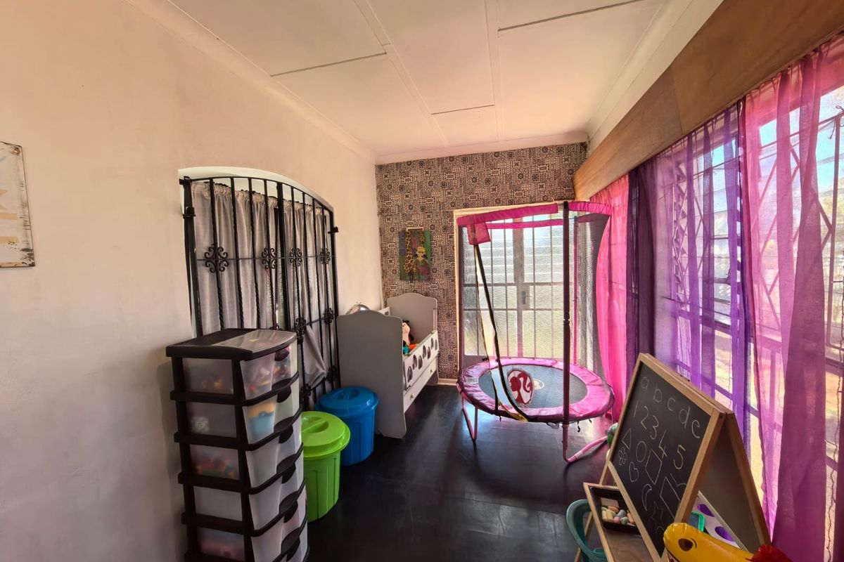 A bedroom featuring dark flooring, patterned accent wallpaper, and security bars on the windows and internal doorway.