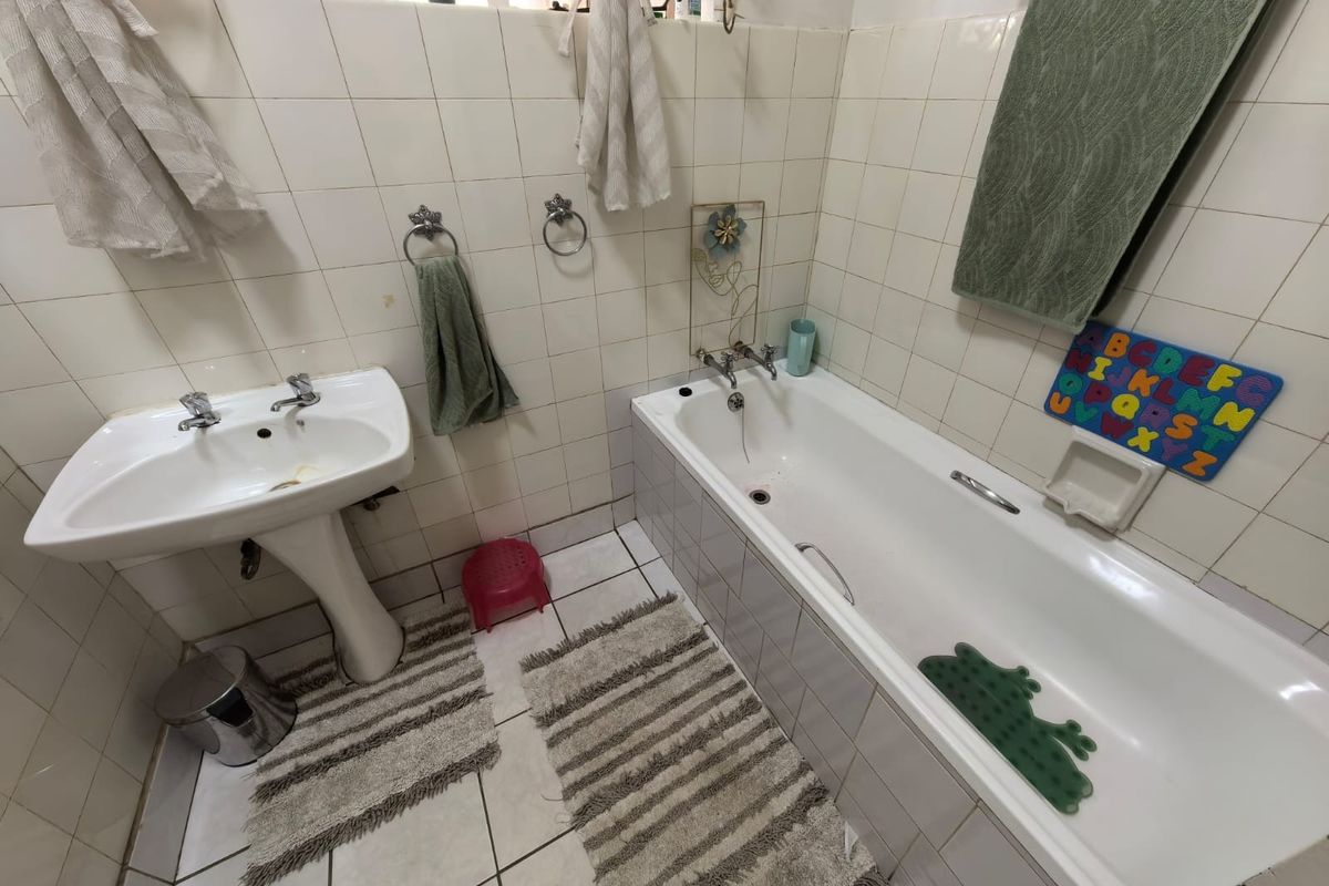 A functional family bathroom featuring a white pedestal basin, bathtub, and full-height ceramic wall tiling, requiring cosmetic updates to modernize the space.