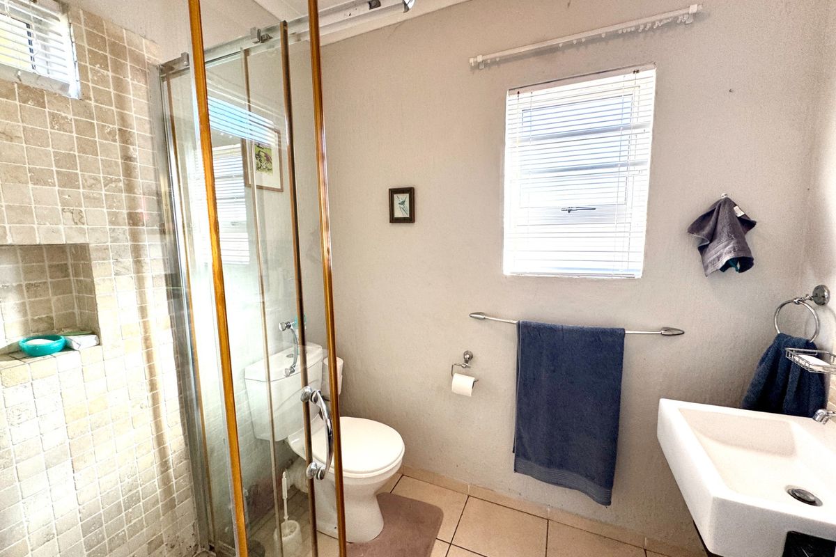 Functional bathroom featuring a glass-enclosed shower with tiled niche, wall-mounted basin, and tiled flooring, offering a practical layout with natural light.