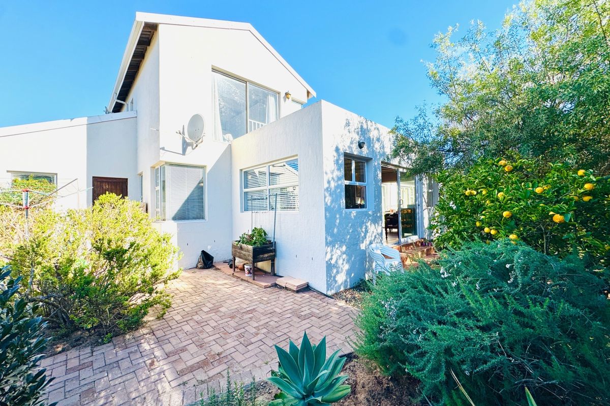 Rear view of the property featuring a brick-paved patio area, established garden, and sliding glass door access to the interior living space.