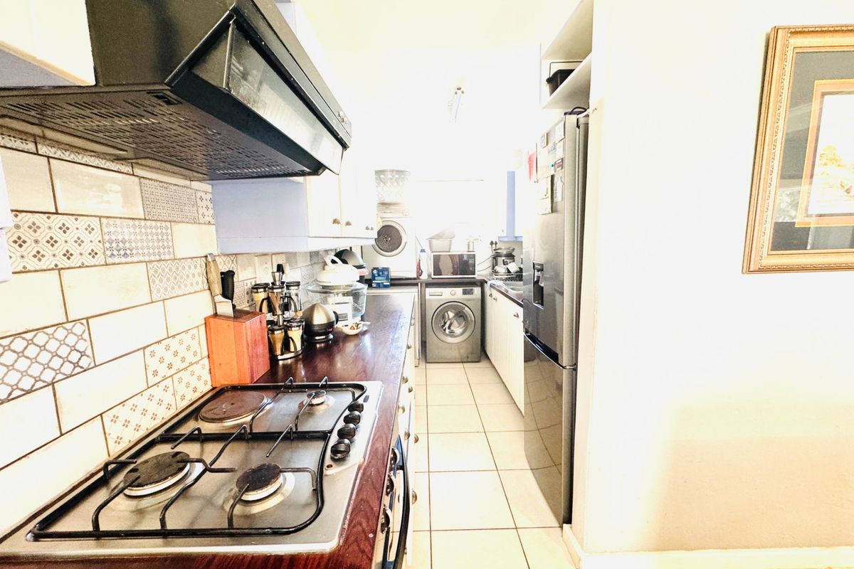 A functional galley-style kitchen featuring a gas hob, extractor fan, decorative tiled backsplash, and integrated laundry facilities with tiled flooring throughout.