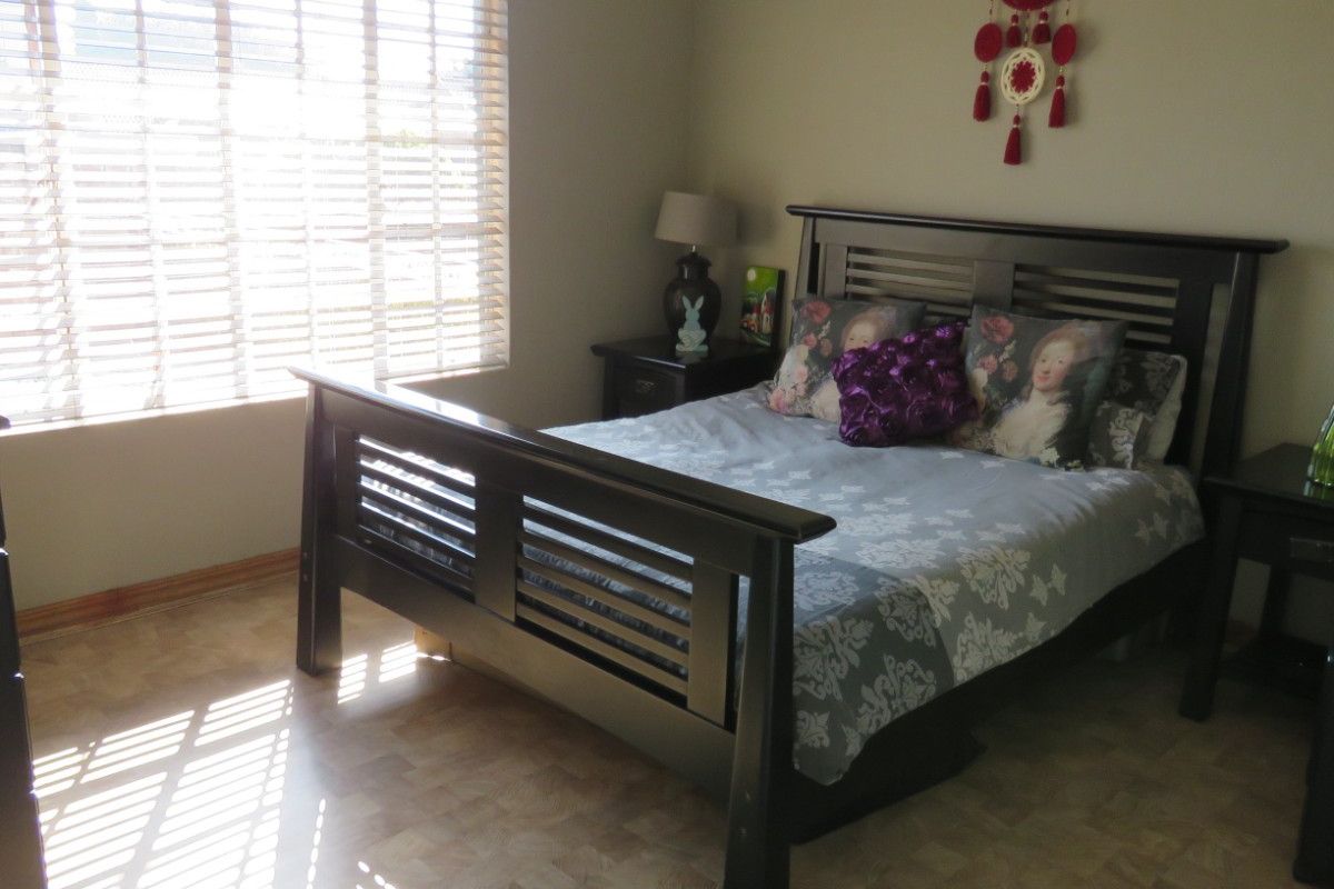A well-lit bedroom featuring neutral wall tones, vinyl flooring, and horizontal window blinds, providing a comfortable and functional living space.