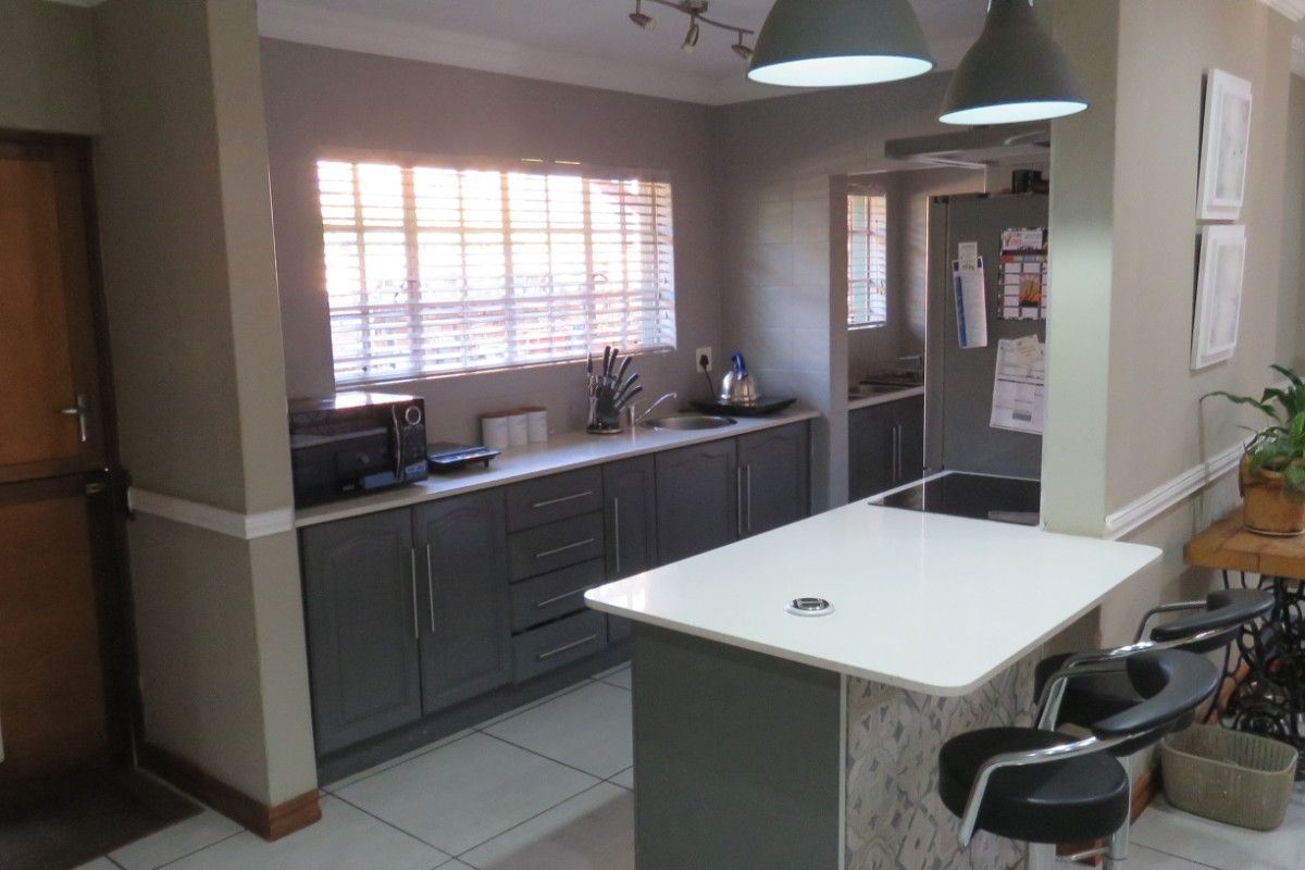 Modern kitchen featuring a central island with breakfast bar, sleek grey cabinetry, tiled flooring, and integrated lighting, adjacent to a functional scullery area.