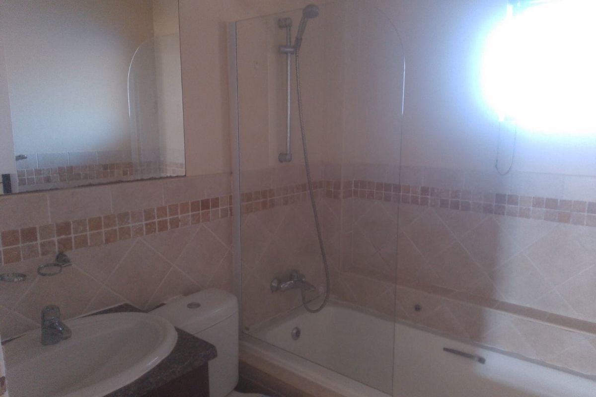 A functional bathroom featuring a built-in bathtub with a glass shower screen, a vanity basin, and neutral wall tiling.
