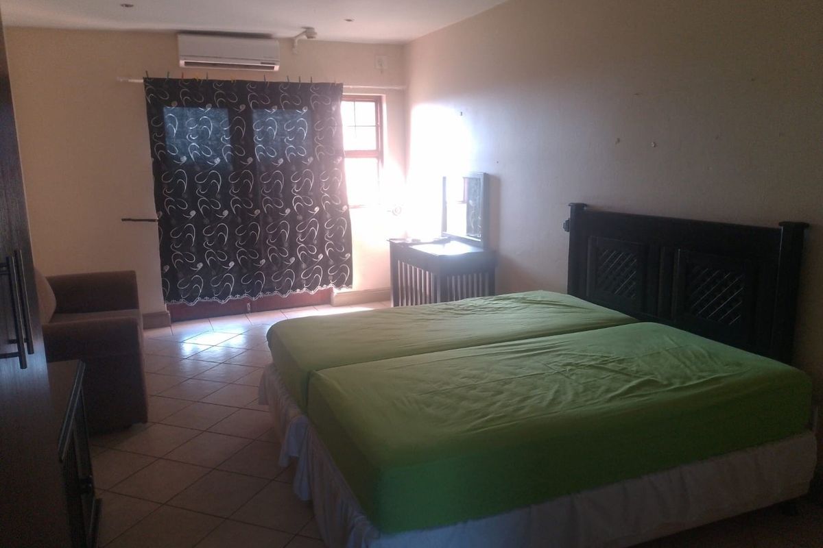 A spacious bedroom featuring tiled flooring, a wall-mounted air conditioning unit, and large windows allowing natural light into the room.
