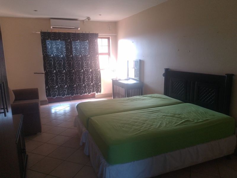 A spacious bedroom featuring tiled flooring, a wall-mounted air conditioning unit, and large windows allowing natural light into the room.
