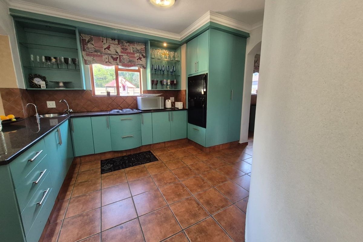 A functional kitchen featuring teal cabinetry, granite countertops, built-in oven, ceramic hob, and tiled flooring with a classic backsplash.