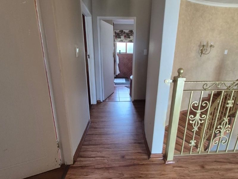 A bright hallway featuring laminate flooring and a decorative metal balustrade, leading towards a bathroom area.