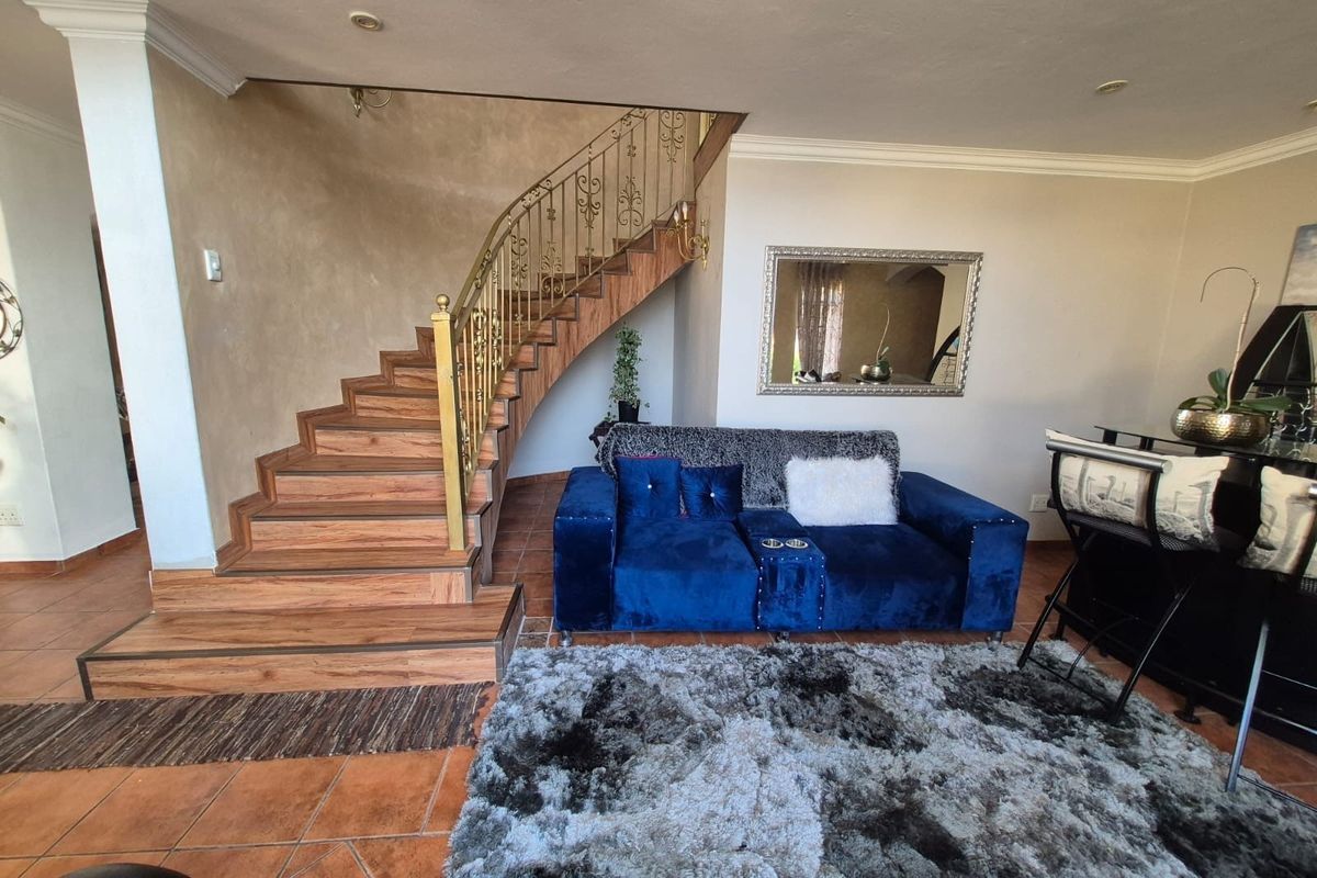 Living room area featuring a wooden staircase with a decorative metal balustrade and terracotta-style floor tiling.