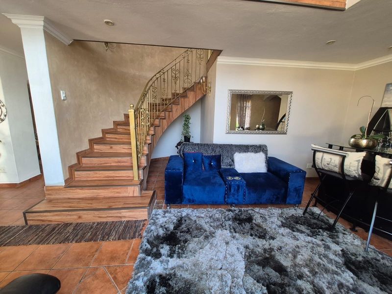 Living room area featuring a wooden staircase with a decorative metal balustrade and terracotta-style floor tiling.