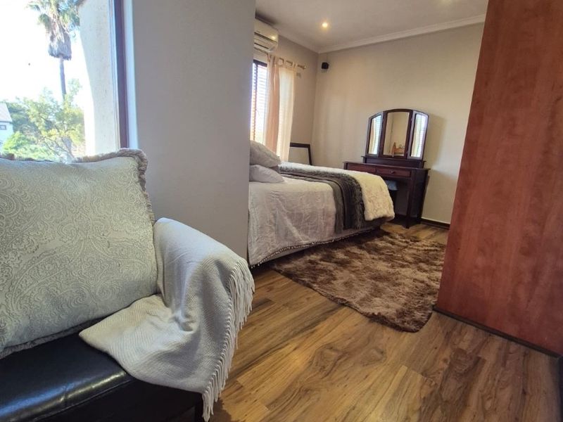 Spacious bedroom featuring warm laminate flooring, recessed downlighting, an integrated air conditioning unit, and large windows providing natural light.