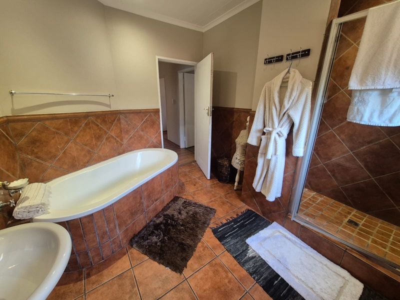 A functional bathroom featuring a built-in bathtub, separate shower enclosure, and warm-toned ceramic wall and floor tiling.