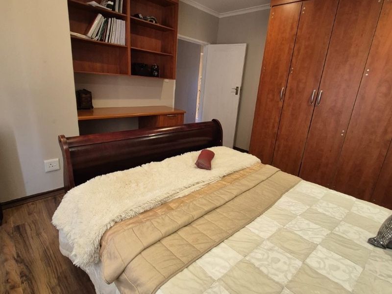 A well-maintained bedroom featuring warm-toned laminate flooring, extensive built-in wooden cabinetry, and a dedicated built-in desk with integrated shelving.