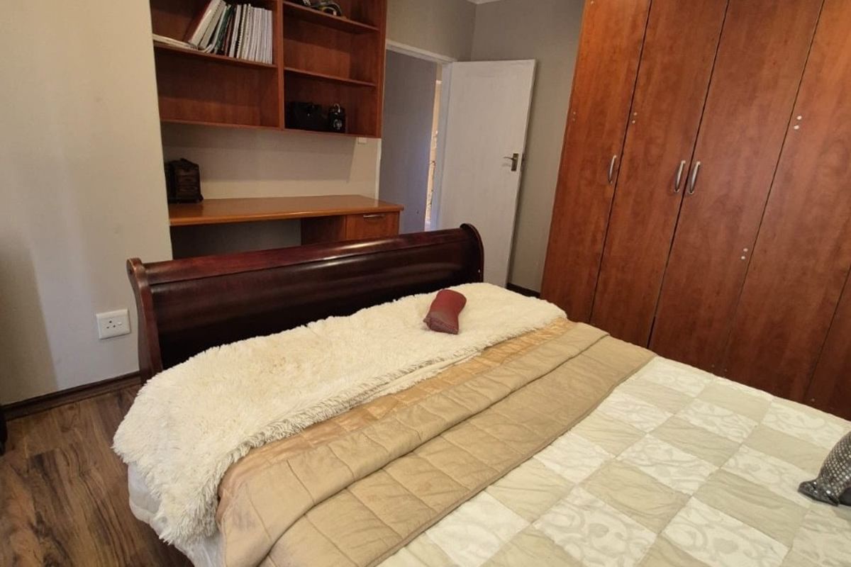 A well-maintained bedroom featuring warm-toned laminate flooring, extensive built-in wooden cabinetry, and a dedicated built-in desk with integrated shelving.