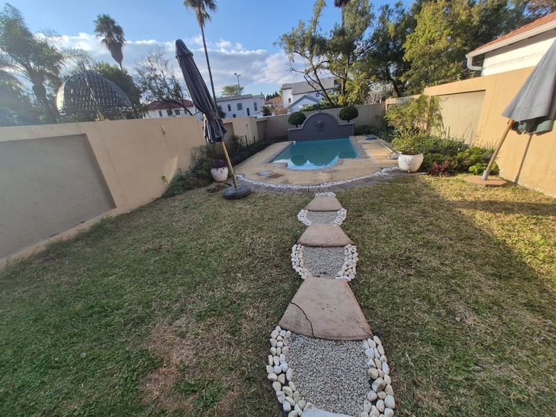 A private backyard featuring a swimming pool with a stone water feature, surrounded by a boundary wall and a decorative stone pathway.