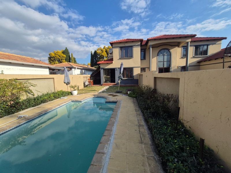 Rear exterior view featuring a swimming pool with tiled surround, perimeter boundary walls, and a two-story house facade with a tiled roof.