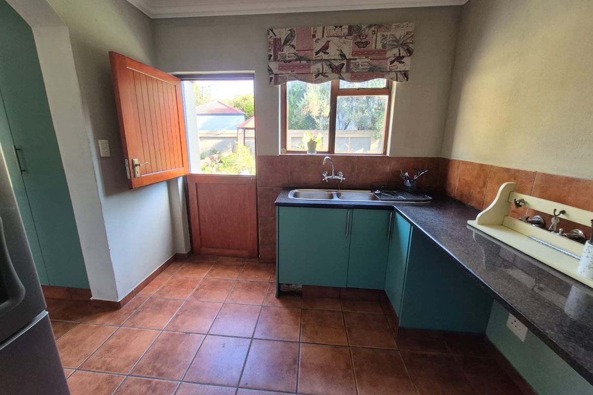 A functional kitchen area featuring tiled flooring, dark countertops, built-in cabinetry, a double sink, and a stable-style door leading to the exterior.