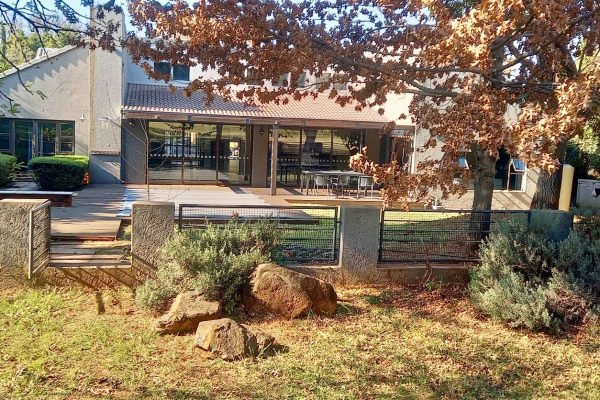 Rear view of the property featuring a covered patio, wooden decking, and a landscaped garden area with established trees and stone retaining walls.