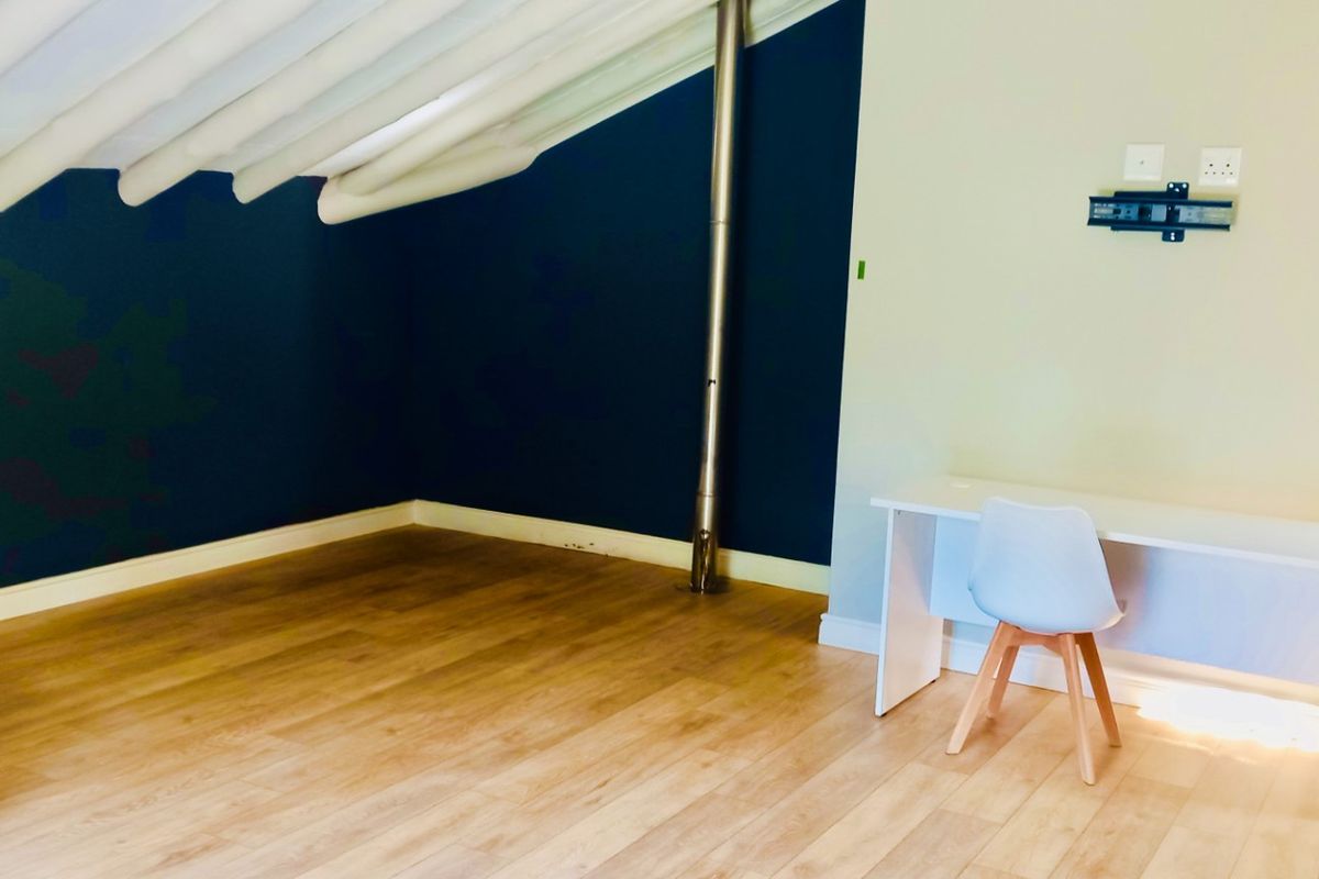 A spacious bedroom featuring vaulted ceilings with exposed beams, wood-look flooring, and a feature wall with a built-in flue pipe.