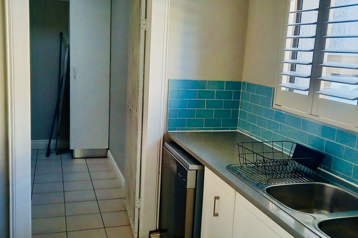 A functional kitchen featuring blue subway tile splashbacks, stainless steel double sink, and integrated dishwasher, leading into a tiled utility area.