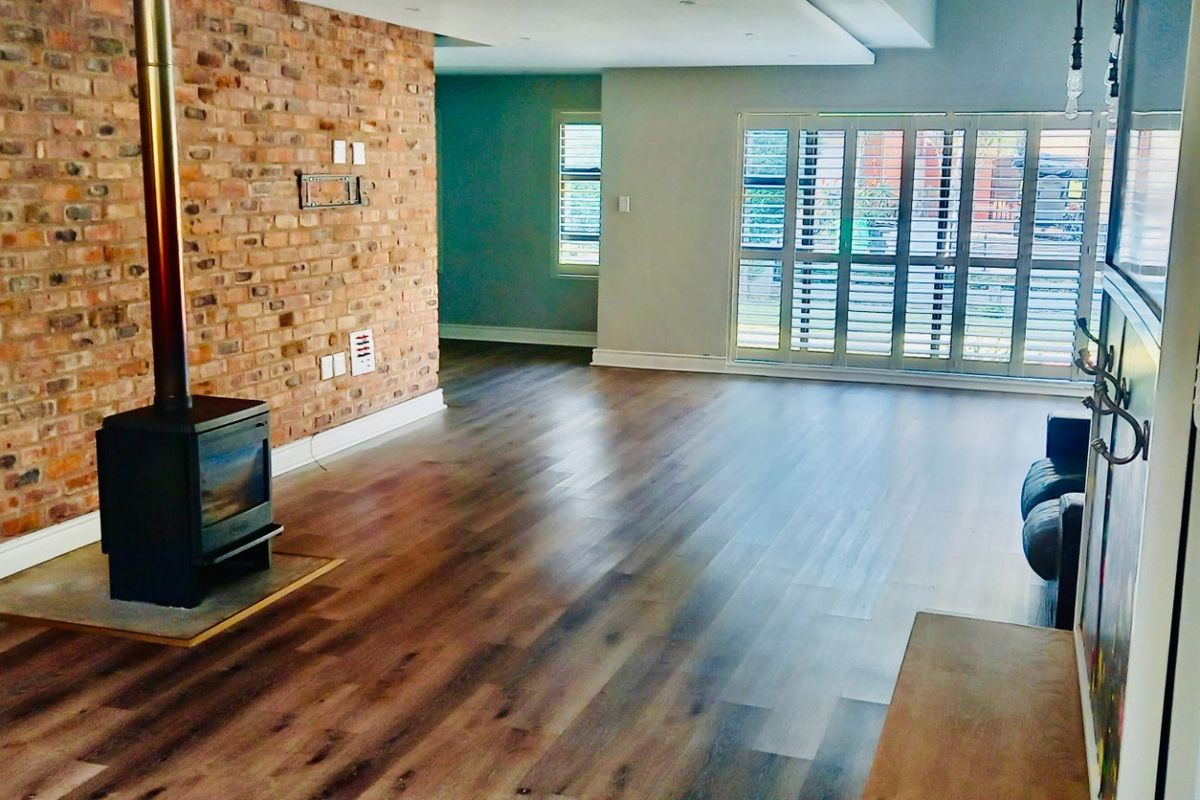Spacious living area featuring a prominent exposed brick feature wall, a built-in wood-burning fireplace, and large windows with fitted shutters.