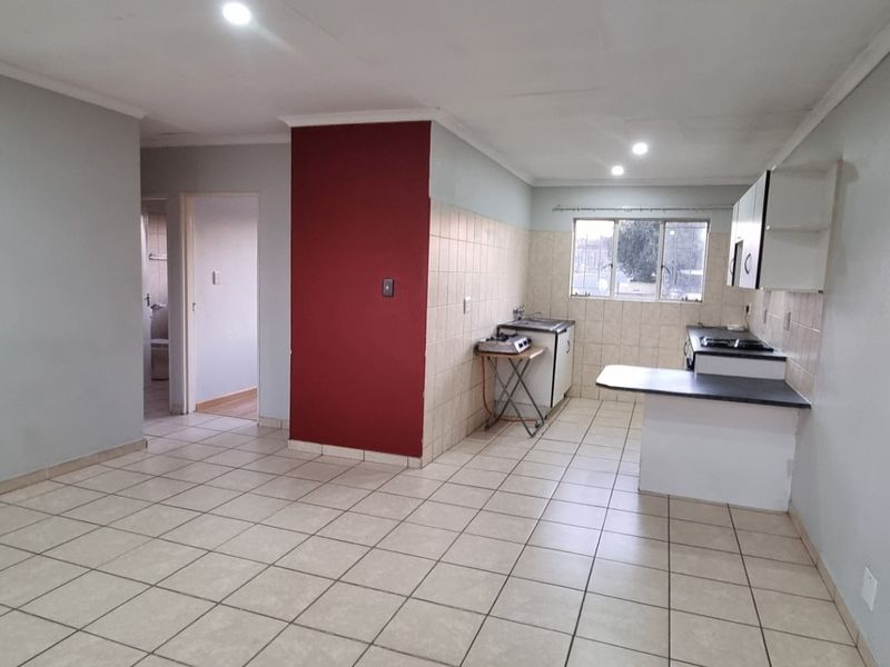 An open-plan living and kitchen area featuring tiled flooring, neutral wall tones, and functional kitchen cabinetry with a breakfast counter.