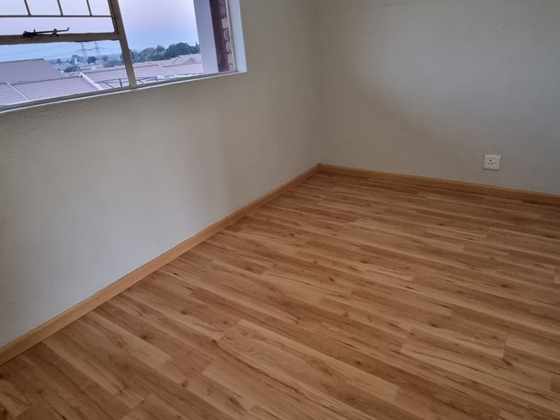 A vacant bedroom featuring laminate flooring, built-in cupboards, and a window with security bars, offering a clean and neutral space.