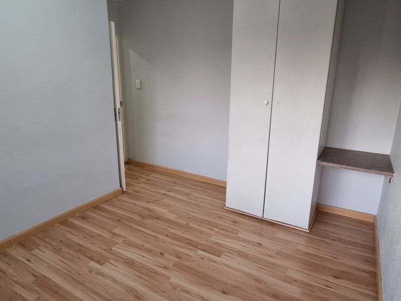 A clean, empty bedroom featuring light laminate flooring, neutral walls, and a built-in wardrobe with an integrated desk area.