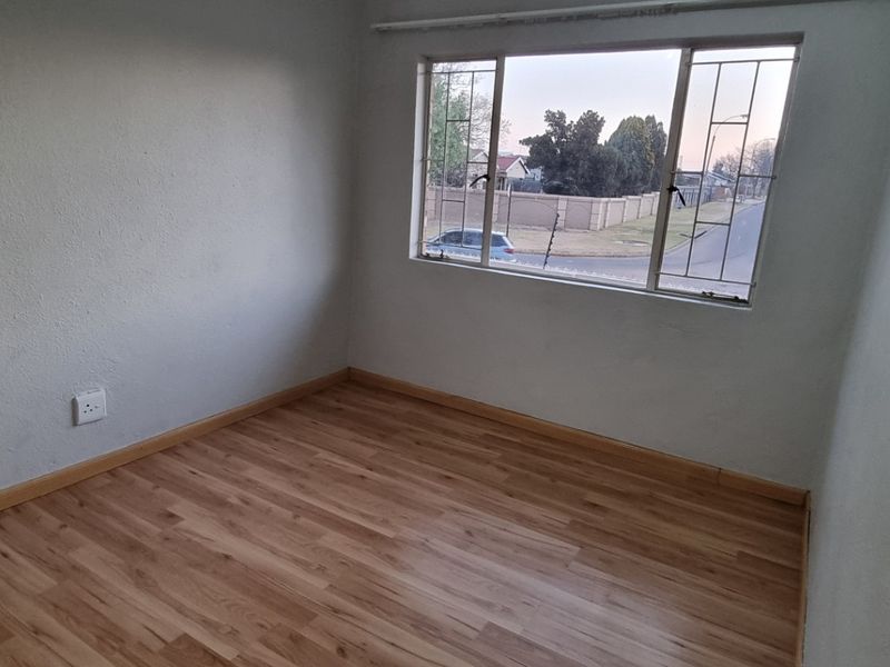 An empty bedroom featuring laminate flooring, neutral walls, and a window fitted with security bars, offering a blank canvas for personalization.