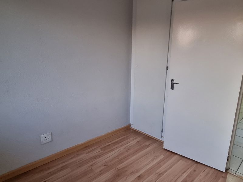An empty bedroom featuring laminate flooring, a built-in cupboard, and a view into an adjacent tiled room.