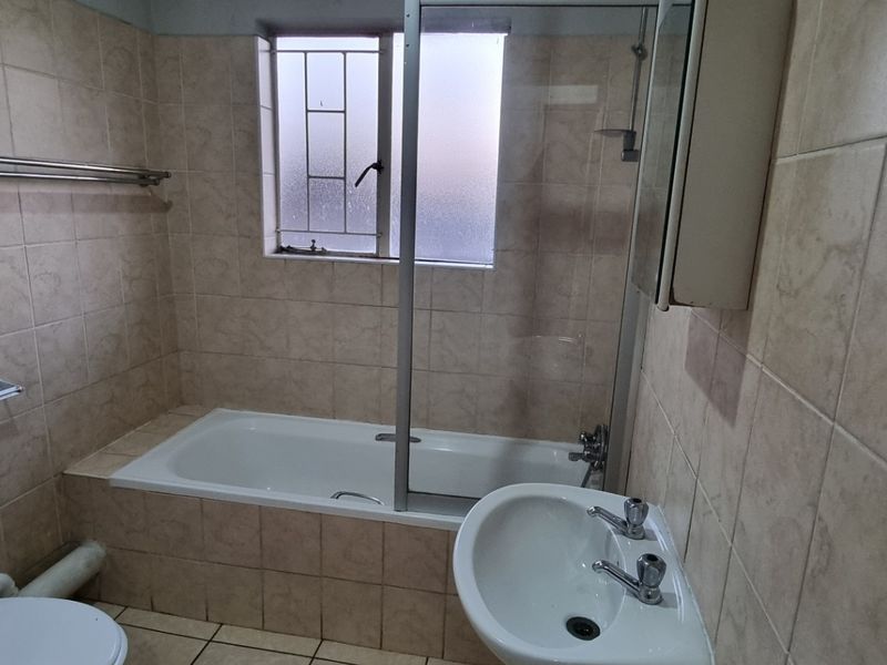 A functional bathroom featuring a bathtub with a shower screen, pedestal basin, and toilet, finished with neutral wall and floor tiling.